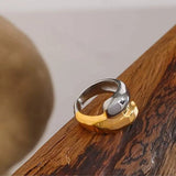 Bague femme acier inoxydable posée sur support en bois, mettant en valeur sa finition brillante et son contraste doré-argent.